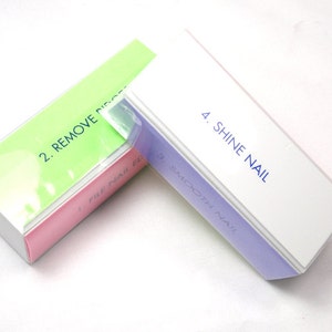 Puede incluir: Un buffer de uñas de cuatro lados con instrucciones para cada lado. Los lados están etiquetados como "1. File Nail", "2. Remove Ridges", "3. Smooth Nail" y "4. Shine Nail". El buffer está hecho de plástico blanco con una superficie rosa, verde y morada.