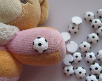 Può includere: Primo piano di un orsacchiotto con corpo rosa e arancione. L'orso indossa un ciondolo a forma di pallone da calcio. L'immagine mostra anche una varietà di ciondoli a forma di pallone da calcio bianchi con cuciture nere.