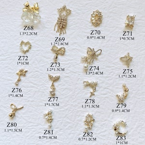 Op de afbeelding: Assortiment van 13 gouden nagelcharms met verschillende ontwerpen, waaronder sterren, strikken, harten, kruisen en manen. De charms zijn versierd met heldere strass steentjes en parels. De charms zijn gelabeld met hun maat in centimeters.