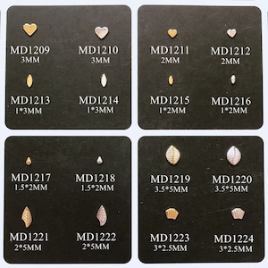 May include: Assortment of 12 gold and silver metal charms in various heart and leaf shapes. The charms are arranged in a grid on a black background. Each charm is labeled with a product code and size in millimeters.