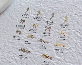 May include: Assortment of gold-toned metal charms in various shapes and sizes, including bows, roses, and words like "Loveme" and "Kissme". The charms are labeled with their size and product code.