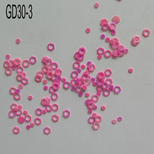 Op de afbeelding: Roze iriserende zeshoekige pailletten verspreid over een witte achtergrond.  GD30-3