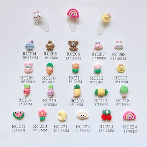 May include: A collection of colorful, miniature resin charms in various shapes, including a bear, bunny, carrot, and rainbow. Each charm has a unique design and is labeled with a code and size in millimeters. These charms are ideal for nail art or craft projects.