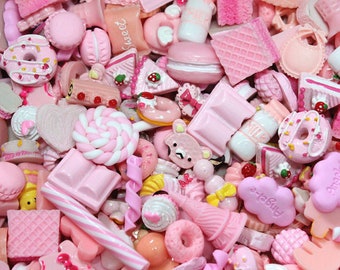 May include: A selection of pink and white miniature food charms, such as donuts, macarons, candy bars, and milk bottles. The assortment showcases diverse textures and shapes, creating a whimsical and playful aesthetic. Suitable for crafting or jewellery making.