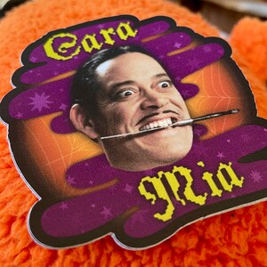 May include: A purple and orange sticker with a cartoon image of a man with a mustache and a paintbrush in his mouth. The text "Cara" and "glia" are written in yellow pixelated letters on the sticker.