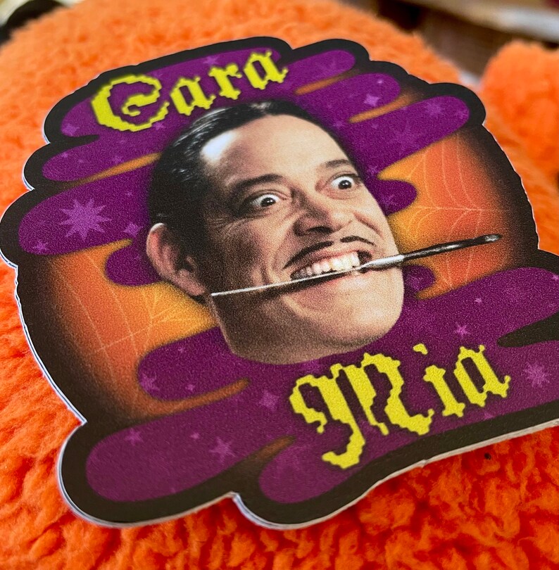May include: A purple and orange sticker with a cartoon image of a man with a mustache and a paintbrush in his mouth. The text "Cara" and "glia" are written in yellow pixelated letters on the sticker.