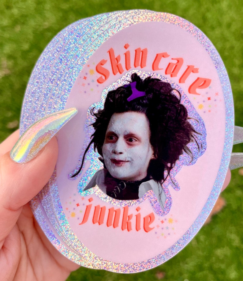 May include: A pink and iridescent glitter sticker with a picture of Johnny Depp as Edward Scissorhands. The sticker says "skin care junkie" in pink and orange letters.