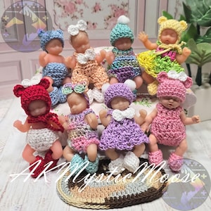 May include: A collection of small baby dolls, each dressed in handmade crochet outfits and hats. The dolls are in various colors, including pink, blue, and yellow. The dolls are arranged on a decorative surface.