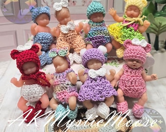 May include: A group of small baby dolls, each wearing handmade crochet outfits and hats. The dolls are in various colours, including pink, blue, and yellow. The dolls are arranged on a decorative surface.