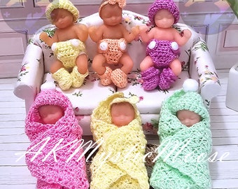 May include: A selection of miniature baby dolls, some seated on a small floral sofa and others wrapped in crocheted blankets. The dolls wear crocheted hats and nappies in pastel shades of yellow, pink, and green.