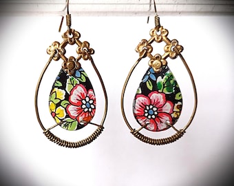 Könnte beinhalten: Handgefertigte Ohrringe mit einem tropfenförmigen Anhänger mit einem Blumenmuster in Rot, Gelb und Blau auf schwarzem Hintergrund. Die Ohrringe haben einen goldfarbenen Metallrahmen und ein gewickeltes Drahtdetail.