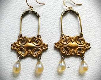 May include: Gold tone earrings with a detailed ornate design and dangling iridescent glass teardrop beads.