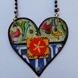 May include: A heart-shaped pendant necklace made from repurposed materials. The pendant is decorated with colorful patterns and a red flower with a yellow center. The necklace is made with a black chain.