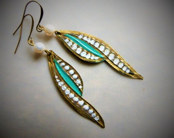 May include: A pair of artisan earrings with a leaf-like design. The earrings feature a gold-colored metal frame, a central turquoise stripe, and white dot accents. Each earring has a small, white pearl and a gold-colored hook.