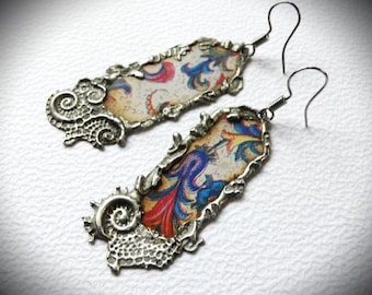 May include: A pair of silver earrings with a floral pattern on the front. The earrings are made of metal and have a hook closure.