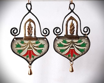 May include: A pair of ornate earrings with a heart-shaped design. The earrings feature a black metal frame with gold accents and a floral pattern in red, green, and gold. A small gold teardrop hangs from the bottom.