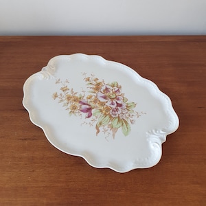 May include: White oval serving tray with a scalloped edge and a floral design in shades of brown, yellow, and purple.