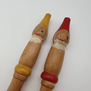 Puede incluir: Dos figuritas de madera de personas con caras pintadas. Una figurita lleva un sombrero amarillo y la otra lleva un sombrero rojo.