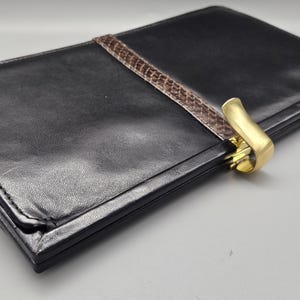 May include: A black leather wallet with a brown snakeskin trim and a gold metal clasp.