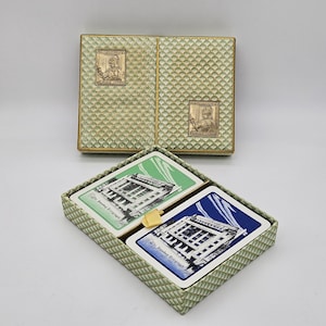 May include: A vintage playing card set with two decks, one green and one blue, each showing a building illustration and the text "The Sunday Telegraph." The set is presented in a decorative box with a textured, light green pattern and two metal relief plaques.