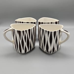 Puede incluir: Juego de cuatro tazas de cerámica blanca con un patrón abstracto en blanco y negro. Las tazas tienen una forma angular única.
