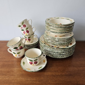 May include: A vintage set of ceramic dinnerware with a green and white floral pattern featuring red plums. The set includes plates, bowls, and cups and saucers.