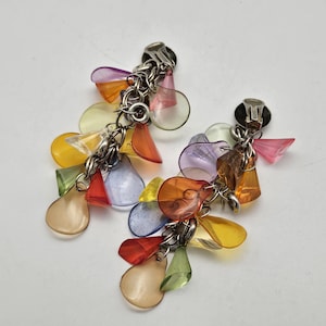 Peut inclure: Une paire de boucles d'oreilles à clip composées de multiples breloques en forme de goutte en plastique translucide de diverses couleurs, dont orange, jaune, violet, rouge, vert et bleu, fixées à des anneaux et des attaches en métal argenté.