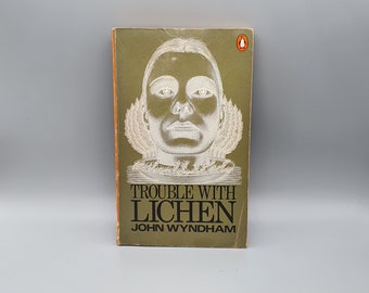 May include: A green paperback book with a white illustration of a person's face on the cover. The title of the book is "Trouble with Lichen" by John Wyndham.