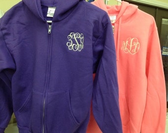 May include: Two hooded sweatshirts, one purple and one coral, with embroidered monograms. The purple sweatshirt has a full zipper and a white monogram. The coral sweatshirt also has a white monogram. Both have front pockets.