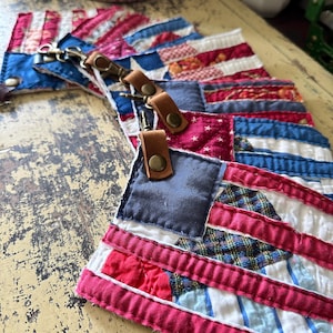 May include: A collection of quilted fabric patches featuring a red, white, and blue flag-inspired design. Each patch is attached to a brown leather strap with a brass-toned metal snap button and a swivel lobster clasp hook.