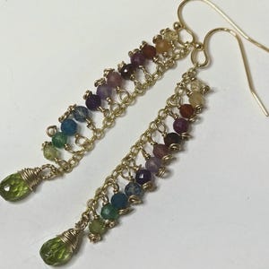 May include: Gold earrings featuring a rainbow of gemstone beads and green teardrop-shaped stones at the bottom.