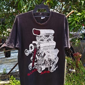 May include: Black t-shirt featuring a detailed engine graphic with the text "HP" and "BAD ASS" in red.