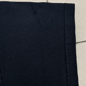 Pu&ograve; includere: Primo piano di un tessuto nero, probabilmente una maglietta o un altro capo di abbigliamento. L'immagine mostra una parte dell'articolo, compresa una cucitura e il bordo del tessuto. Il testo "archive99culture" e le informazioni sulla data sono visibili.