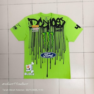 Puede incluir: Camiseta verde lima con diseño de pintura negra goteando. Presenta el logotipo de Monster Energy, el logotipo de Ford y el texto "DC SHOES". Incluye un gráfico de calavera con el número 43 y la palabra "BLOCK".