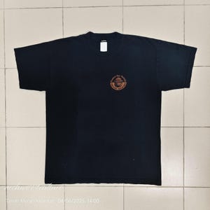 Pu&ograve; includere: T-shirt nera con girocollo e maniche corte. Una grafica circolare sul petto recita "Protect Our Forests, Prevent Wildfires" in un design marrone e arancione. La maglietta &egrave; piatta.