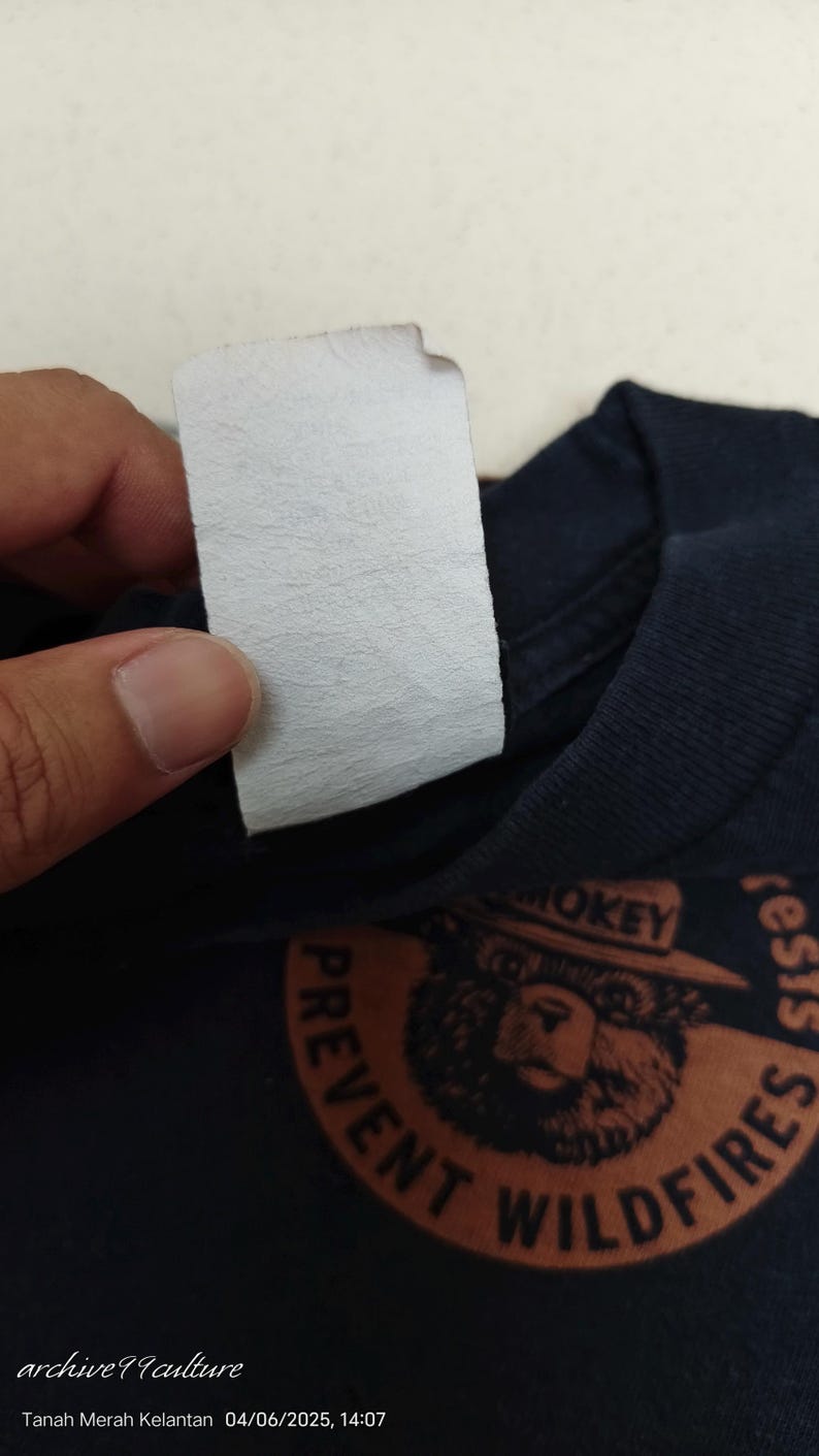 Pu&ograve; includere: T-shirt blu navy con grafica di Smokey Bear e la scritta "PREVENT WILDFIRES". &Egrave; visibile un'etichetta bianca. L'immagine include anche il testo "archive99culture" e la data.