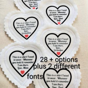 May include: Six white heart-shaped fabric patches with scalloped edges, each featuring black text that reads: This is a shirt I used to wear. Whenever you hold it remember I am there. Love, followed by various names and a small red heart.