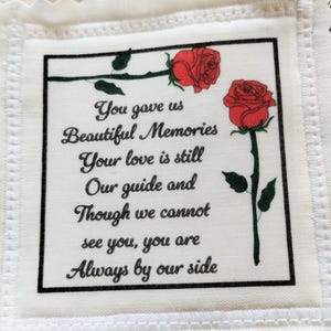 May include: A white fabric square with a black border, featuring the text "You gave us Beautiful Memories Your love is still Our guide and Though we cannot see you, you are Always by our side." Two red roses are also depicted.
