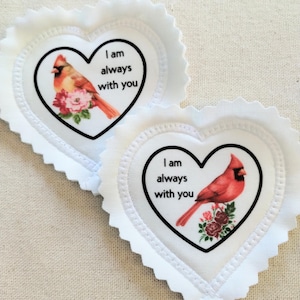 May include: Two heart-shaped white fabric patches with a scalloped edge. Each patch features a red cardinal bird illustration with the text "I am always with you". The bird is perched on a floral arrangement.