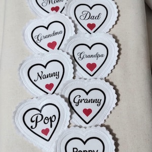 May include: White heart-shaped decorations with scalloped edges, each featuring a black heart outline and a red heart accent. The decorations are labeled with names like "Mom," "Dad," and "Grandma."