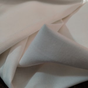 May include: White fabric with a smooth texture, folded in a triangular shape. The fabric is soft and appears to be lightweight.