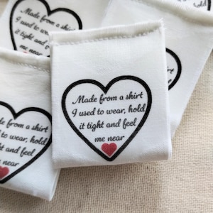 May include: White fabric labels with a black heart design and the text "Made from a shirt I used to wear, hold it tight and feel me near." A small red heart is at the bottom. Several labels are visible.