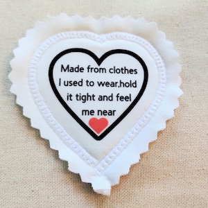 May include: A white heart-shaped fabric patch with pinked edges. The center features a black heart outline containing the text: Made from clothes I used to wear, hold it tight and feel me near, with a small red heart icon below the text.