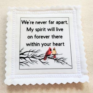 May include: White square fabric with scalloped edges. The center features text: "We're never far apart, My spirit will live on forever there within your heart." Below the text is a branch with two red and yellow birds.