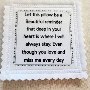 May include: A white square pillow with a scalloped edge and embroidered text. The text reads, "Let this pillow be a Beautiful reminder that deep in your heart is where I will always stay. Even though you love and miss me every day."