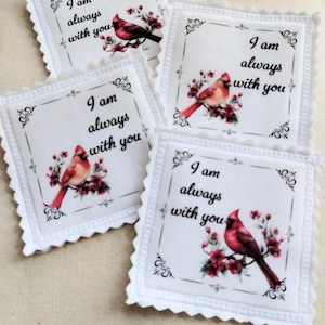 May include: Four white fabric coasters with scalloped edges. Each coaster features a red cardinal bird perched on a flowering branch, with the text "I am always with you" in black script. Decorative corner flourishes frame the text.