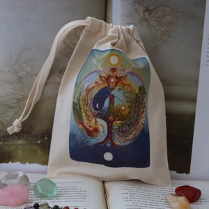 May include: A white drawstring bag with a colorful illustration of a tree, a deer, and the moon. The bag is on a book with the text "Free Range Fairies" and a website address.