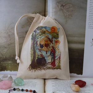 May include: A small, white drawstring bag with a colorful illustration of a fairy scene. The bag is sitting on a book with a crystal necklace and several colorful stones.