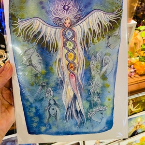 Puede incluir: Una pintura de acuarela de una mujer con alas y una serpiente de colores arco&iacute;ris envuelta alrededor de su cuerpo. La mujer est&aacute; rodeada de otras figuras y s&iacute;mbolos, incluyendo un sol y una luna. La pintura est&aacute; sobre un fondo blanco.