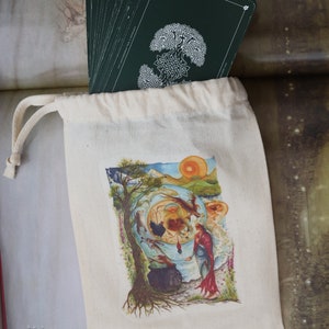 May include: A white canvas bag with a drawstring closure, containing a deck of cards with a green back. The cards feature a white illustration of a tree with a Celtic knot design. The bag has a colorful illustration of a scene with a tree, a woman, and a cauldron. The text "FREE RANGE FAERIES" is printed on the bag, along with the website "www.freerangefaeries.co.uk".